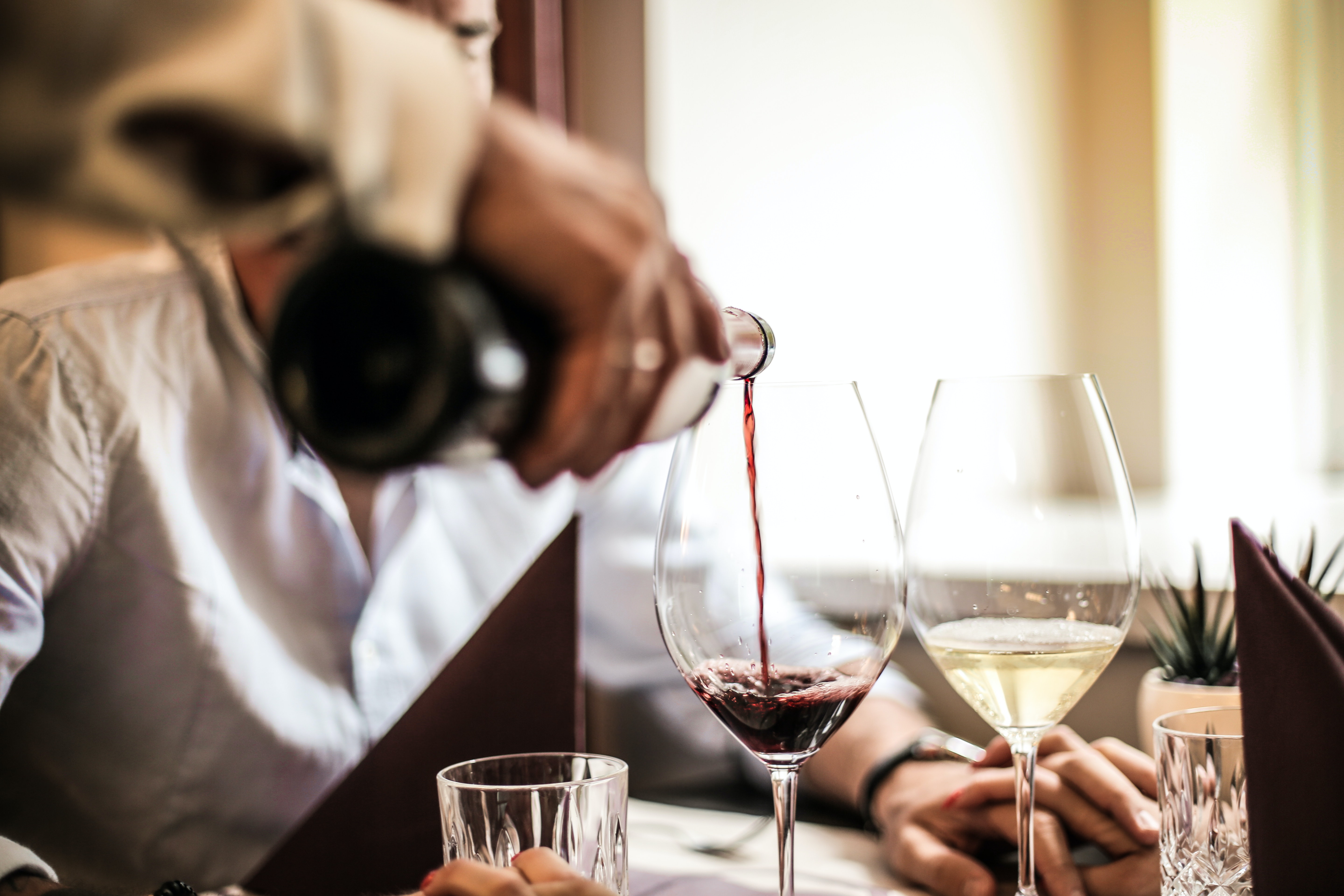An einem Restauranttisch werden von einem Kellner roter und weißer Wein eingegossen