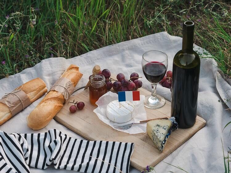 Picknickdecke, auf der Käse, Honig, Weintrauben, Baguette und Wein steht