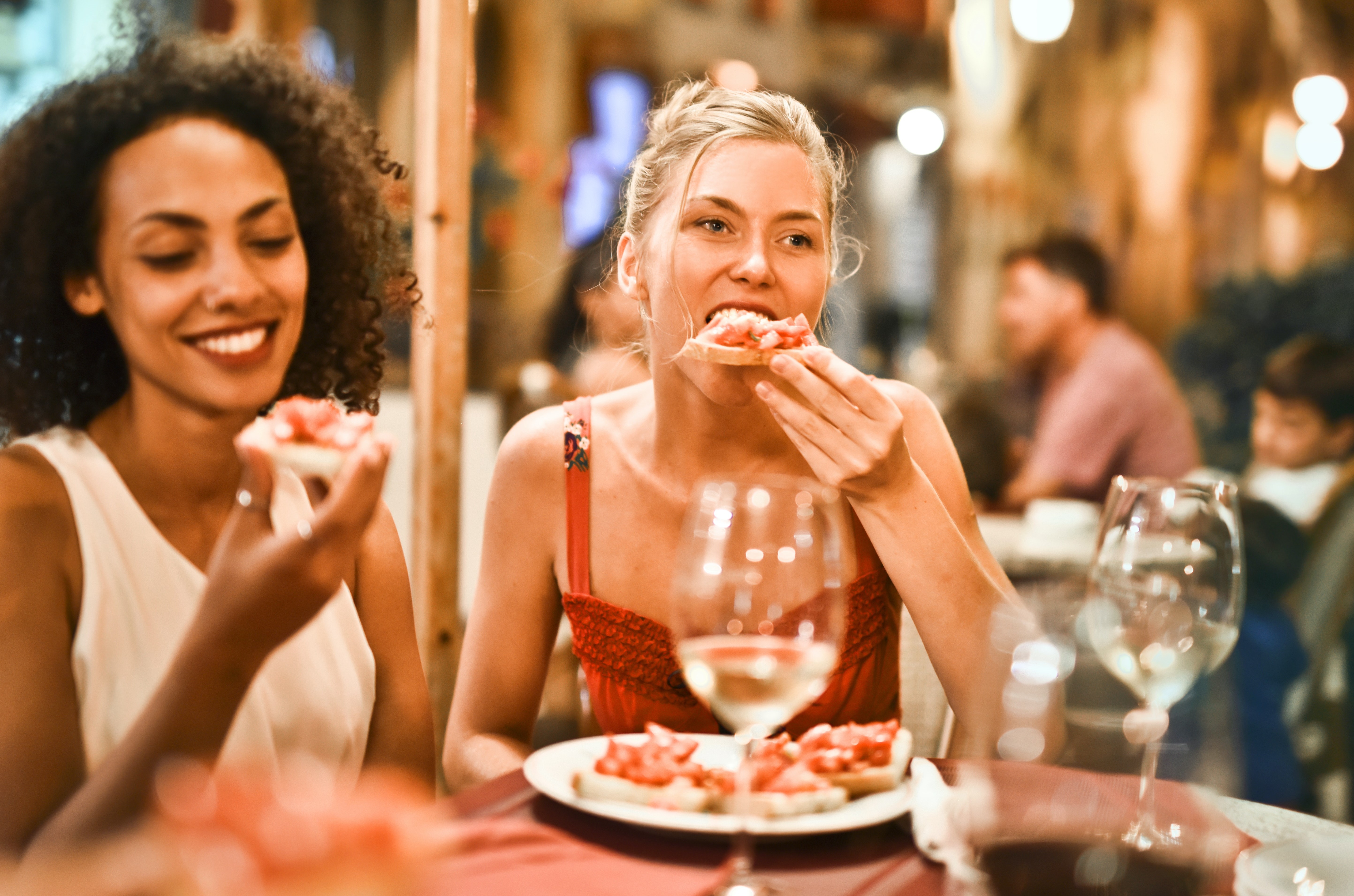 Zwei Frauen genießen zu einem Weißwein Bruschetta und sitzen vor einem Restaurant.
