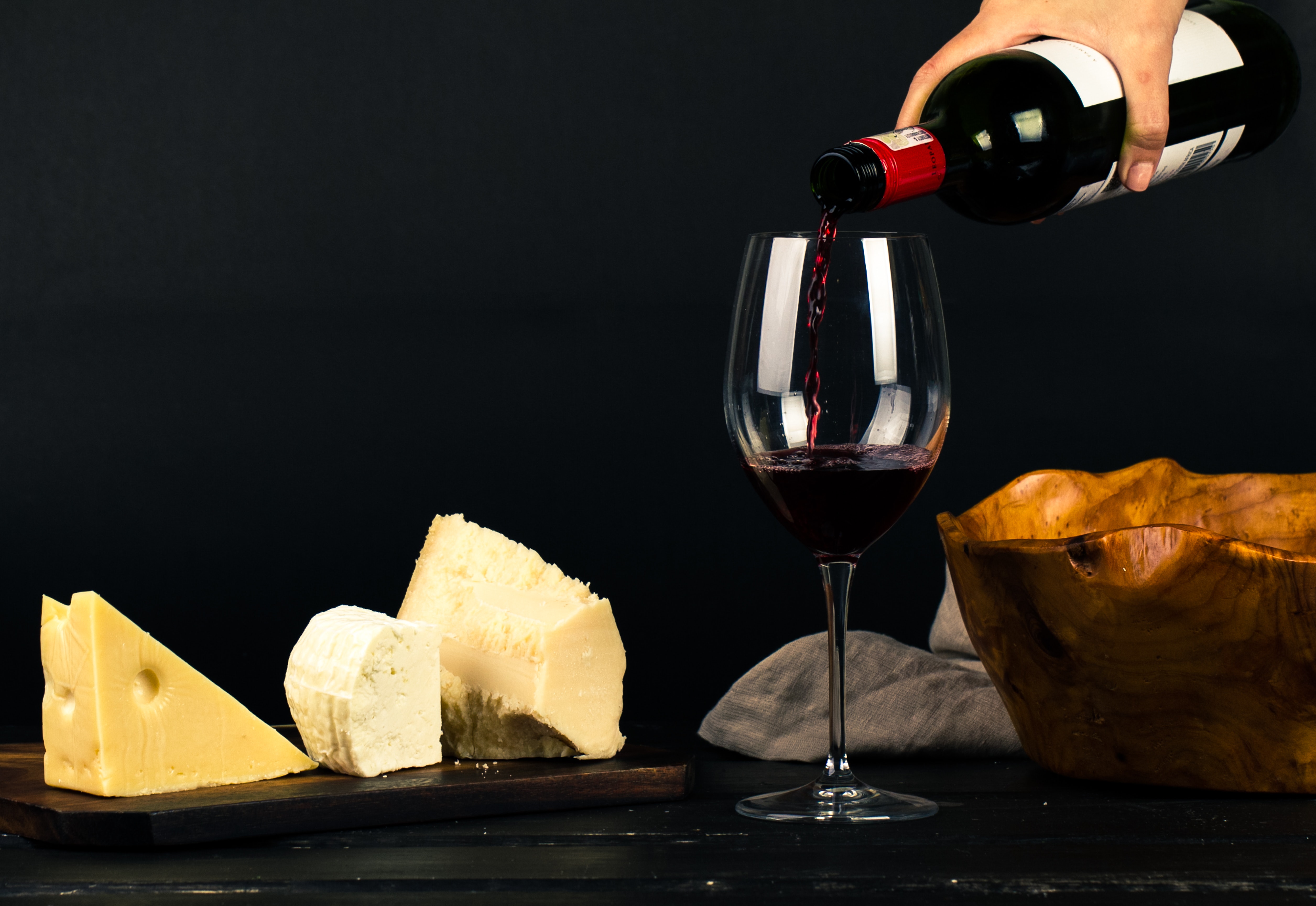 Verschiedene Käsesorten liegen auf einem Brett, daneben wird Rotwein eingegossen.