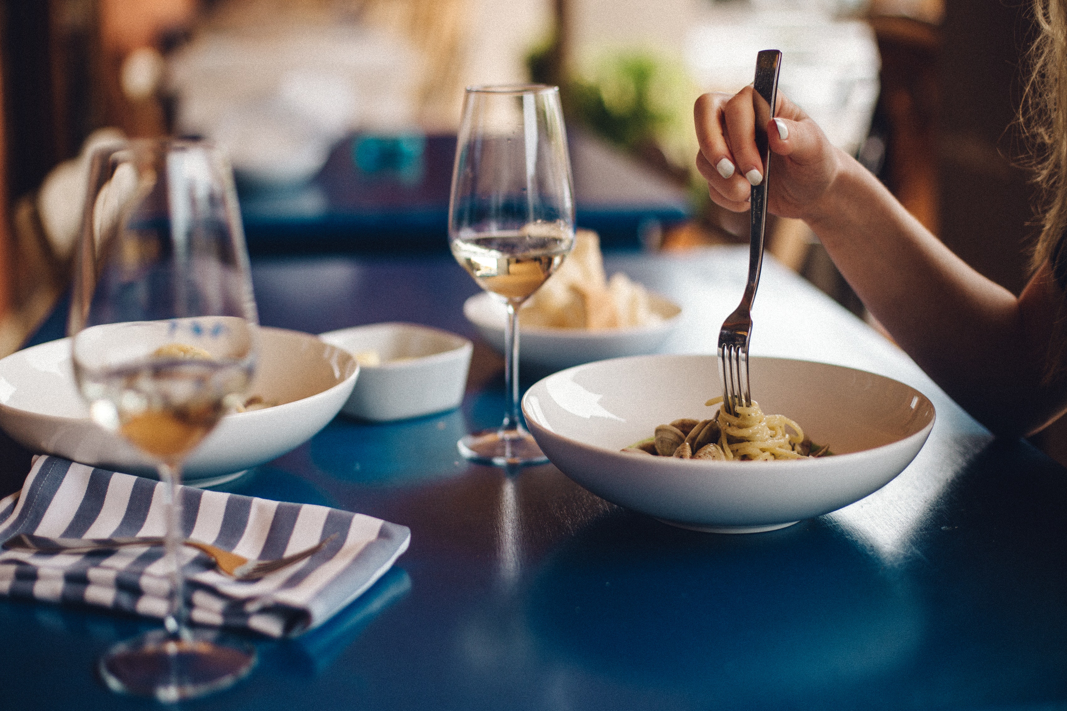 Eine Frau isst Spaghetti mit Meeresfrüchten und trinkt Weißwein an einem blauen Tisch dazu
