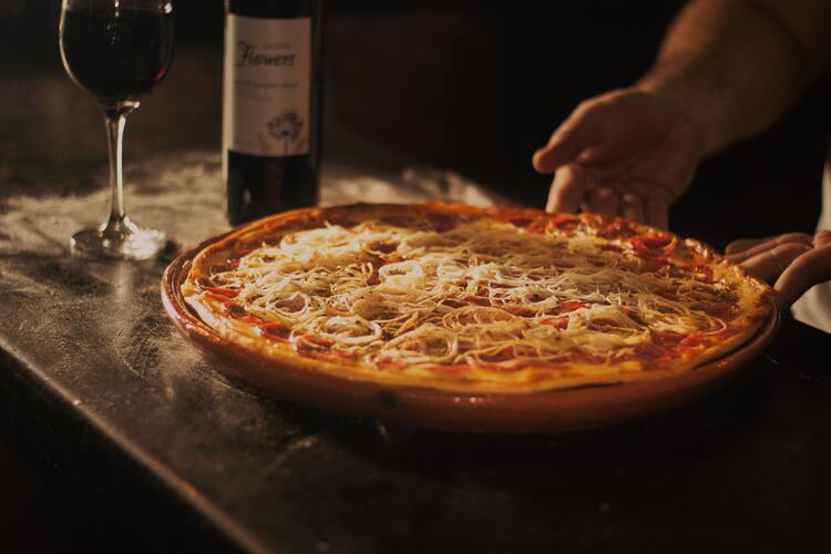 Pizza mit Zwiebeln und Käse - daneben ein Rotwein