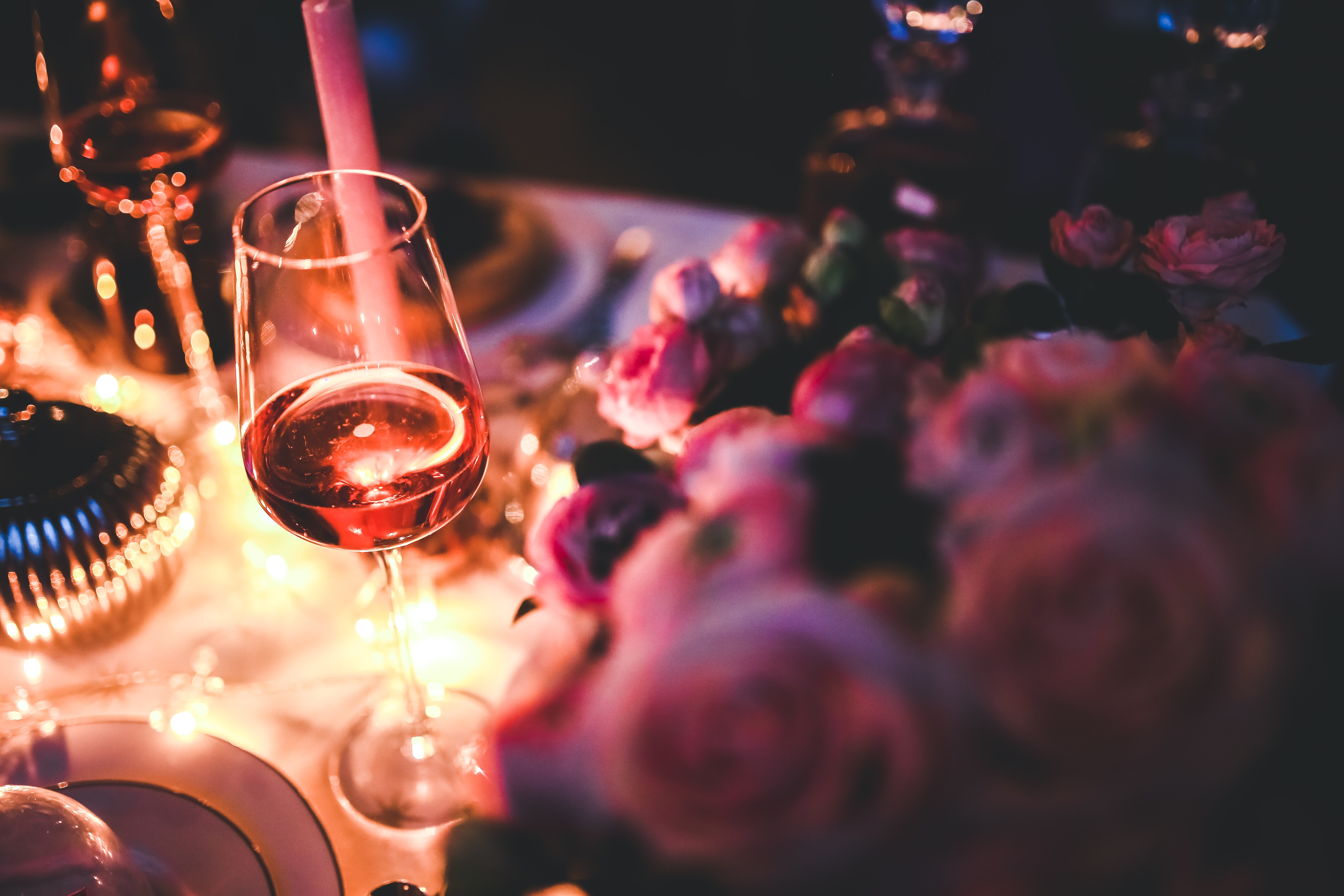 Halbvolles Rosé-Weinglas neben rosafarbenen Rosen und einer Kerze