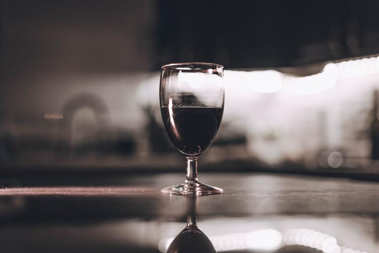 Rotweinglas vor dunklem Hintergrund steht auf spiegelndem Untergrund
