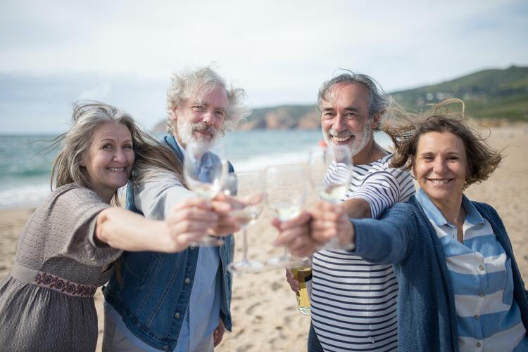 Vier Personen prosten sich mit leeren Weingläsern an einem spanischen Strand zu