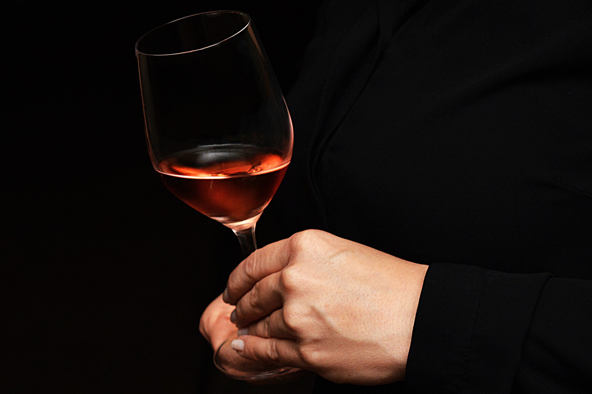 Halbvolles Rosé-Weinglas in der Hand einer Frau, vor schwarzem Hintergund