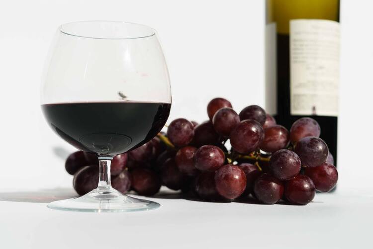 Ein halbvolles Glas Rotwein neben Weintrauben und einer Flasche Wein
