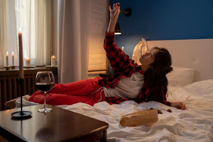 Eine Frau mit einem Weinglas und Pralinen auf einem Bett