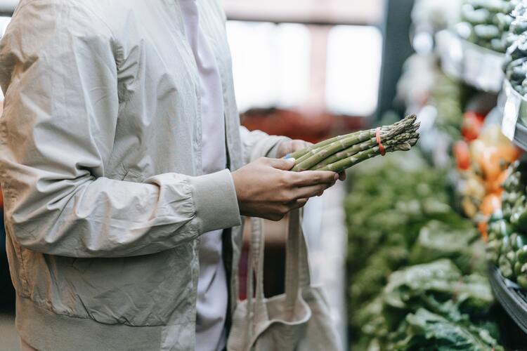 Mann steht in Gemüseabteilung und betrachtet einen grünen Spargelbund