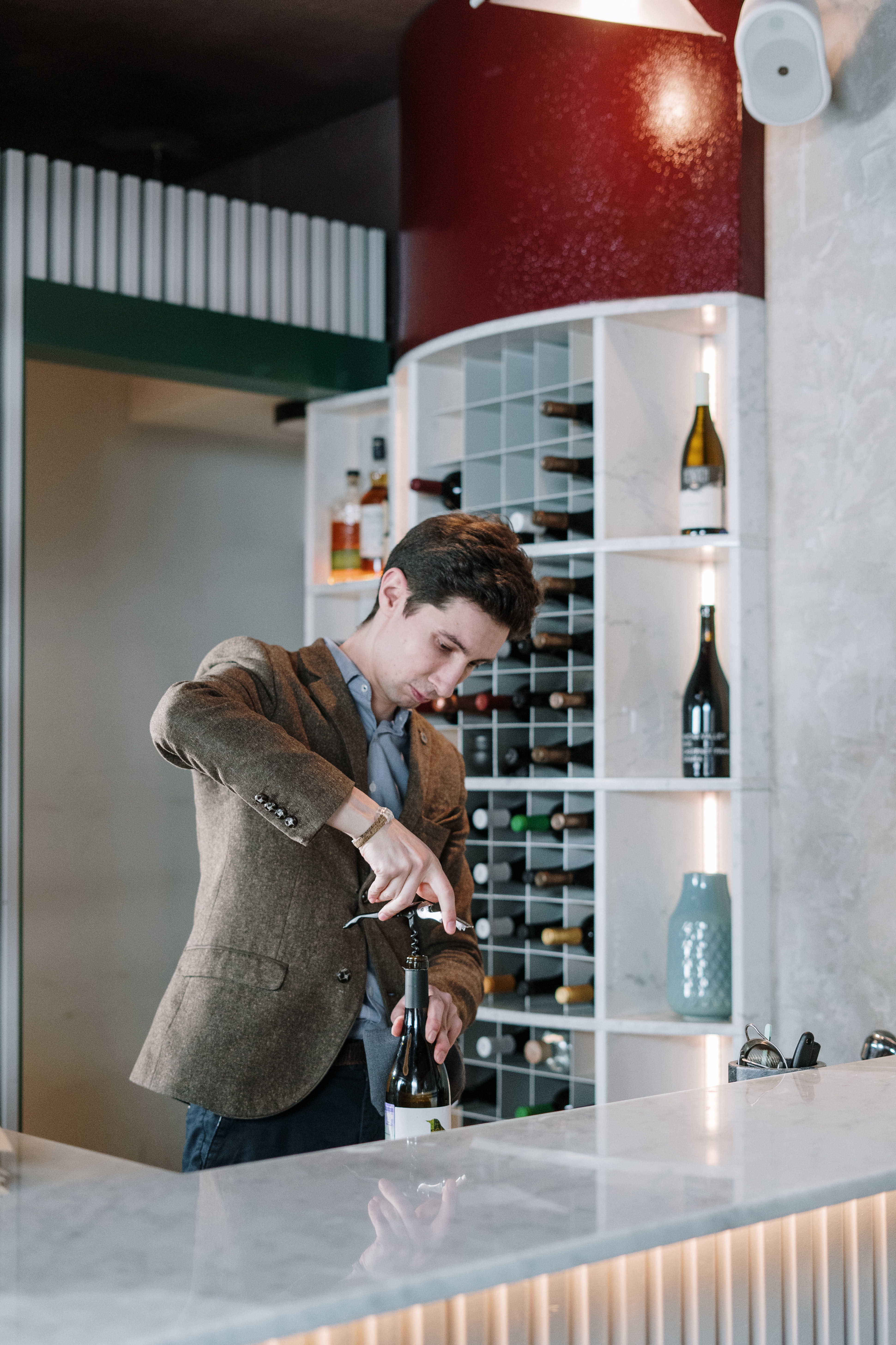 Ein Mann öffnet an einer Bar einen Weißwein mit einem Korkenzieher