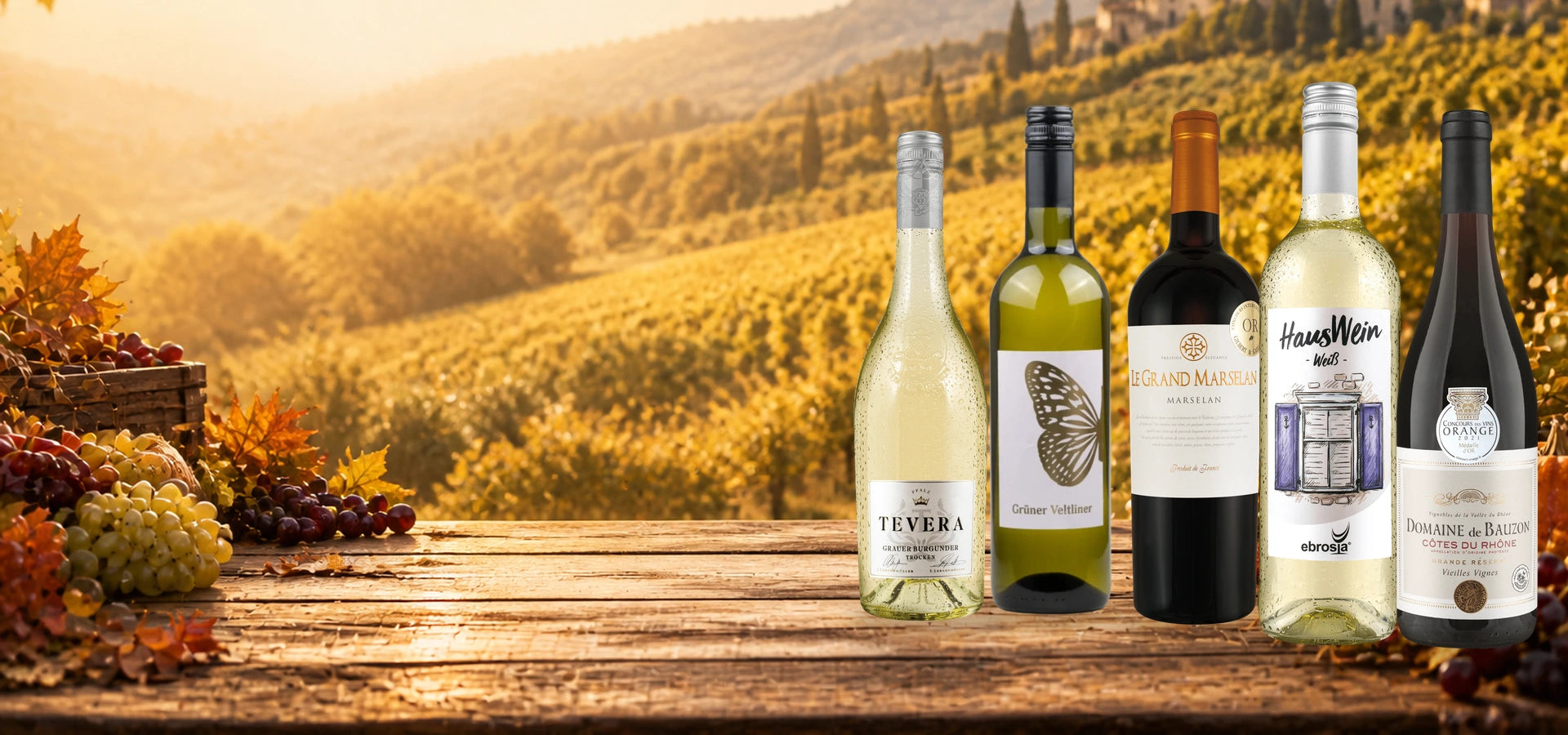 Hauswein Weiß, Domaine de Bauzon, TEVERA Grauburgunder, Grüner Veltliner Schmetterling und Le Grand Marselan als Originalflaschen auf einer herbstlichen Tafel